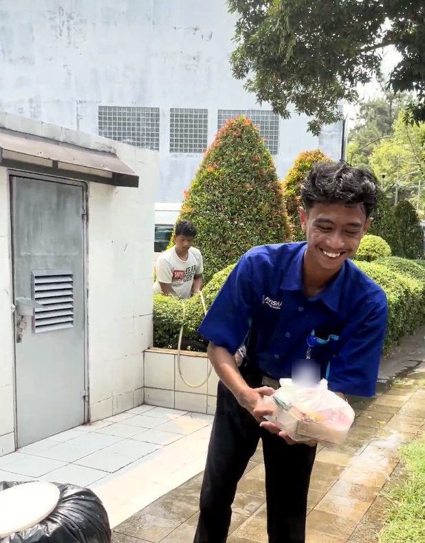 Seorang pekerja berseragam biru tersenyum sambil memegang bungkus nasi