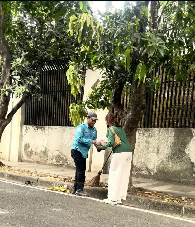 Relawan menyerahkan nasi kotak kepada petugas kebersihan yang sedang memegang sapu di trotoar