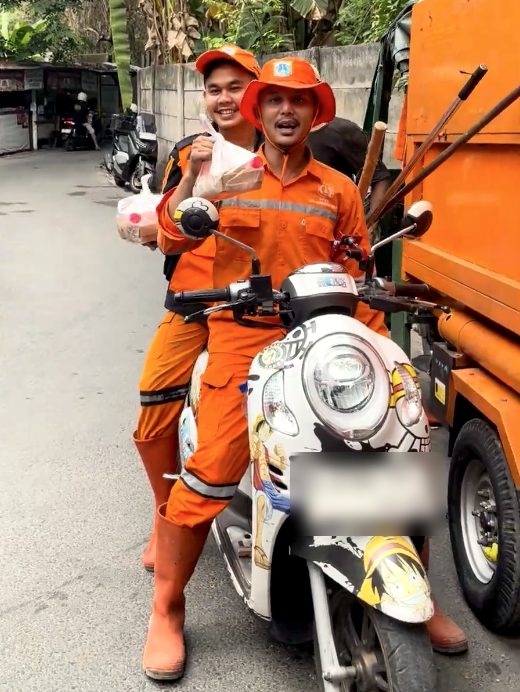 Dua petugas PPSU berseragam oranye tersenyum di atas motor sambil memegang bungkus nasi